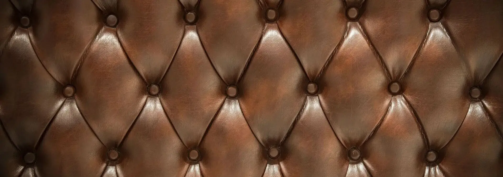 Close-up of a brown, tufted leather upholstery pattern with buttons, forming a diamond-shaped design.