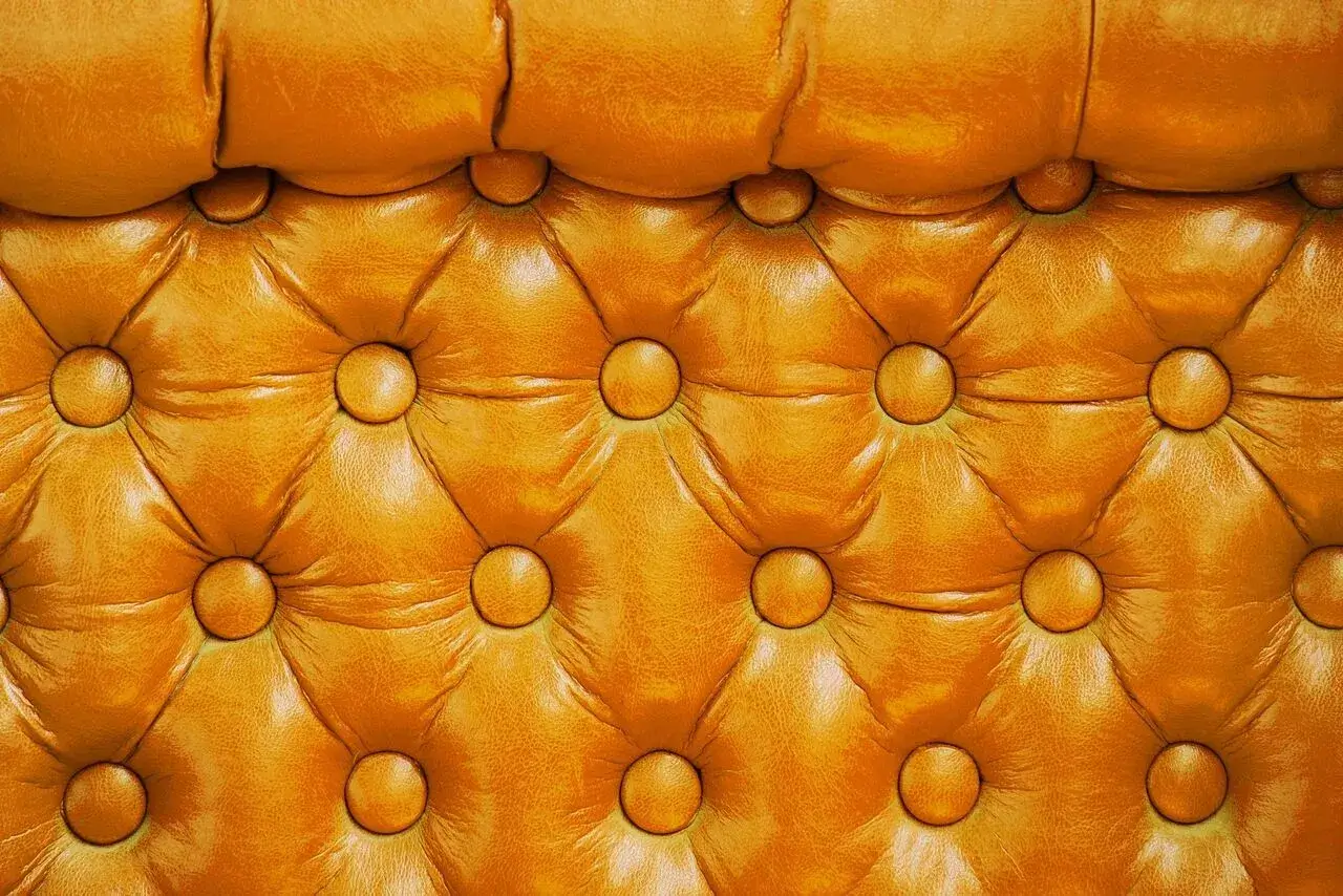 A close-up view of a tufted, mustard yellow leather upholstery, featuring an array of buttons and a textured, padded surface.