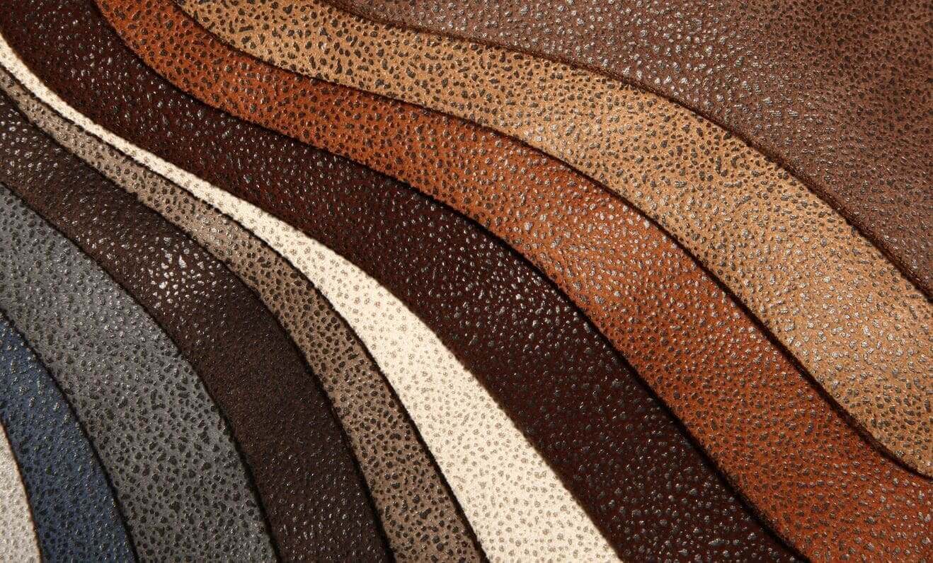 Various shades of textured leather samples arranged in curved, parallel lines, showcasing different colors including brown, beige, and dark gray.