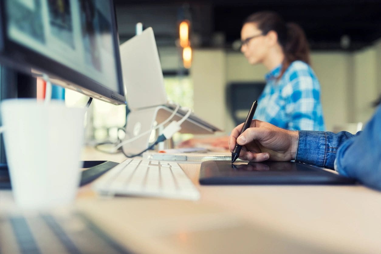 A designer using a graphic tablet next to a computer in an office.